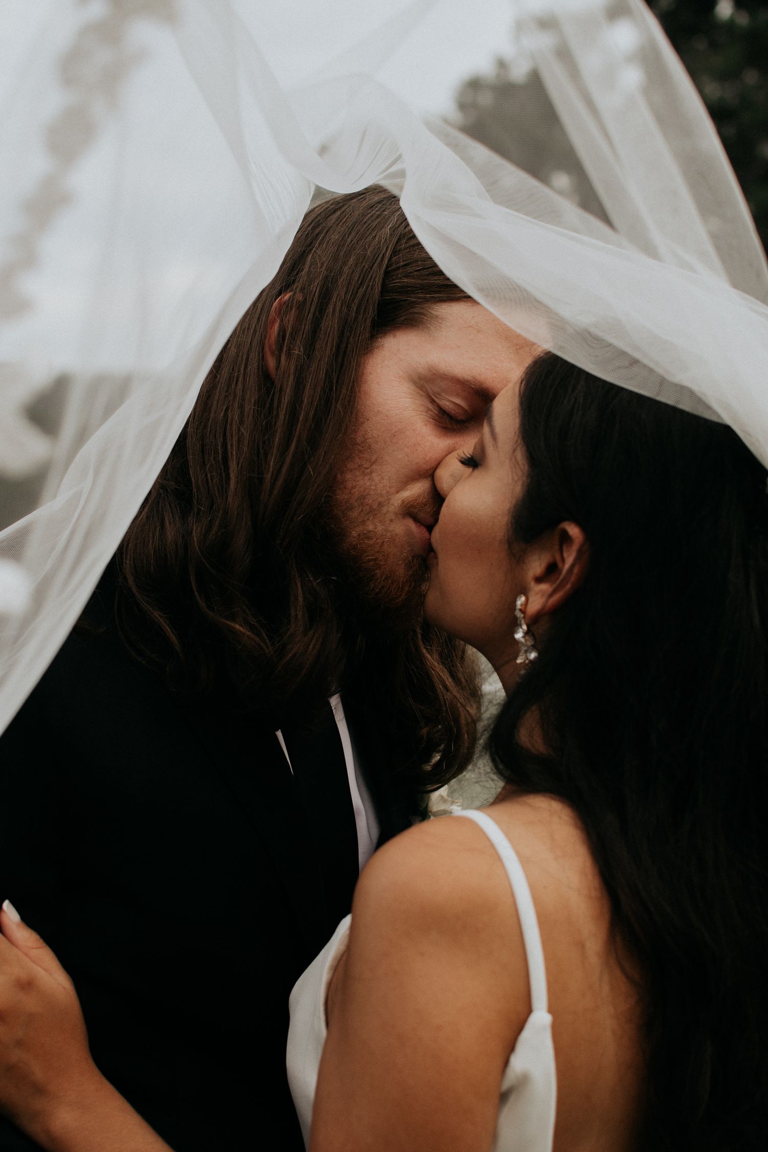 Romantic wedding kiss captured under flowing white veil.