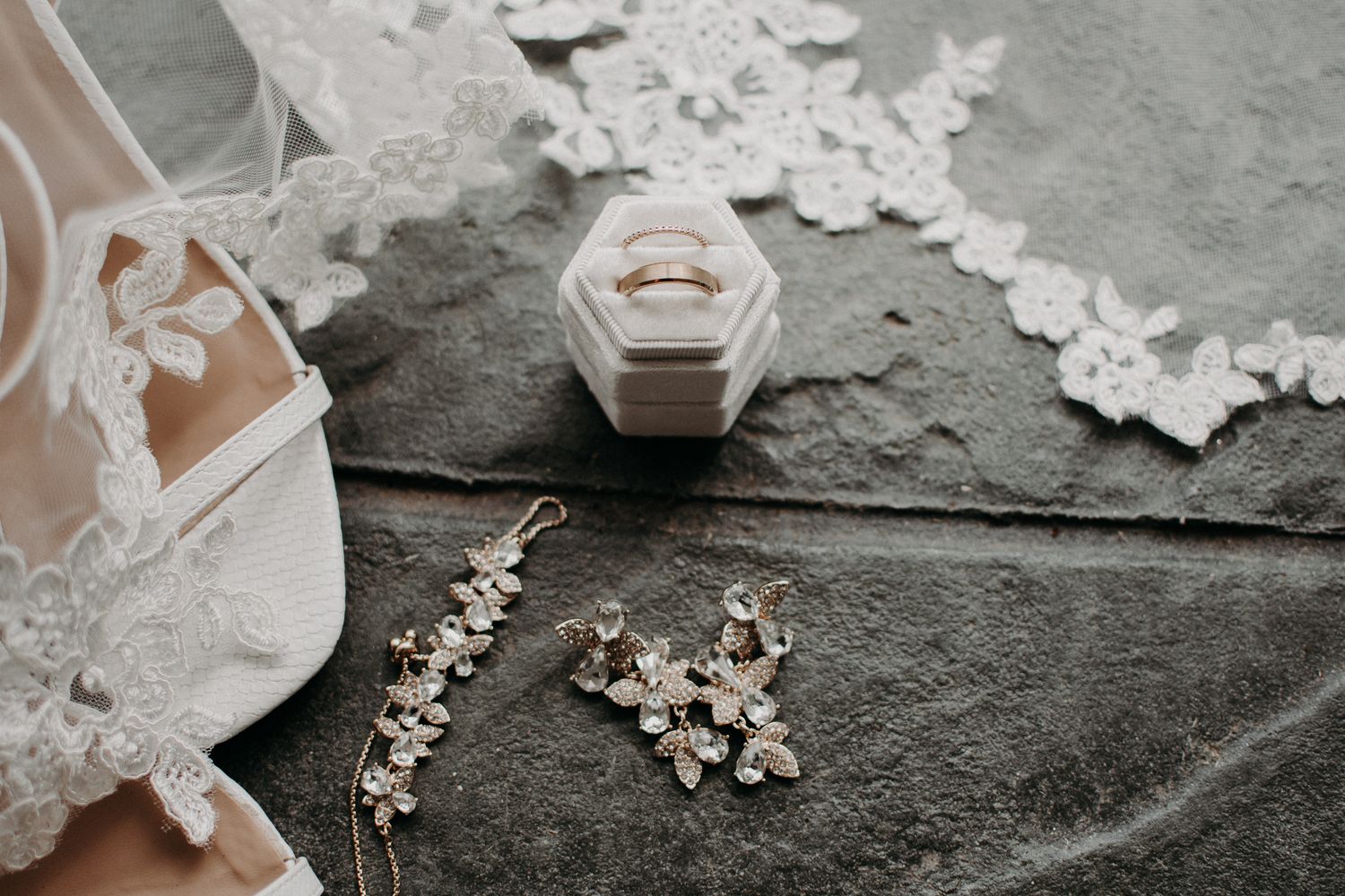 Wedding accessories including rings, earrings and delicate lace details on a gray surface.