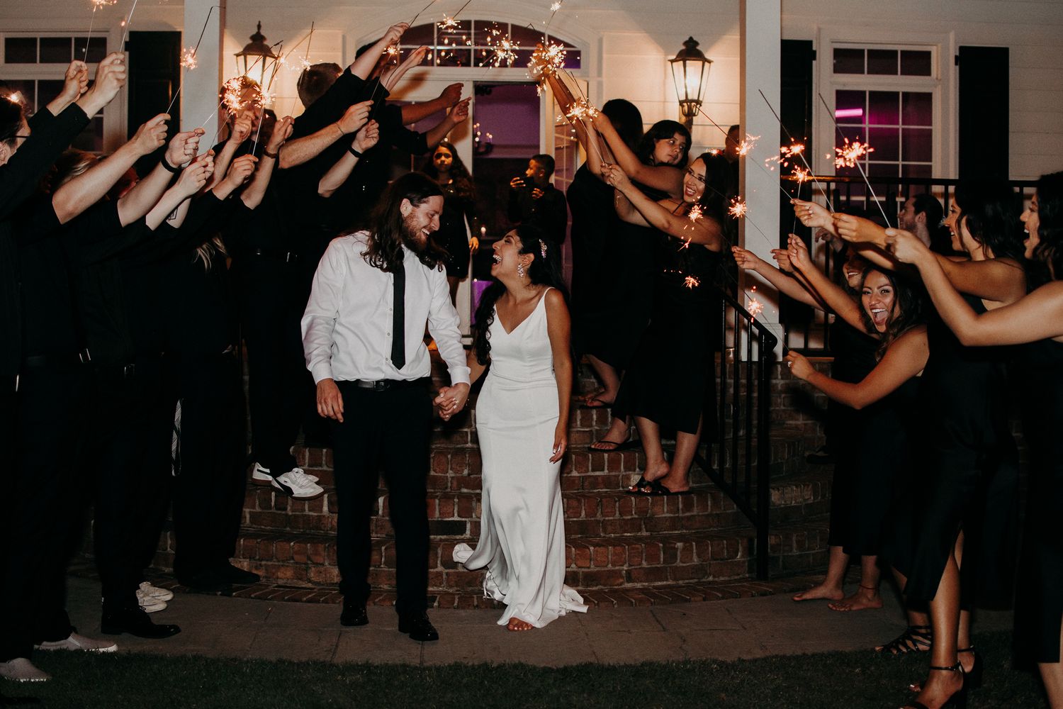 Newlyweds walk through sparkler tunnel exit as wedding guests create magical lighting effect.