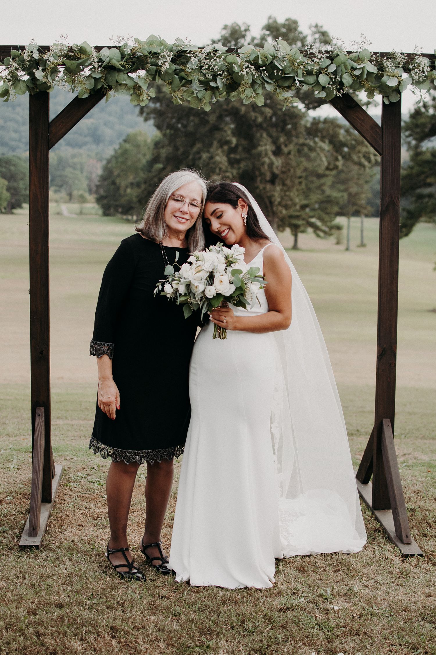 A wedding moment under a wooden arch decorated with greenery.