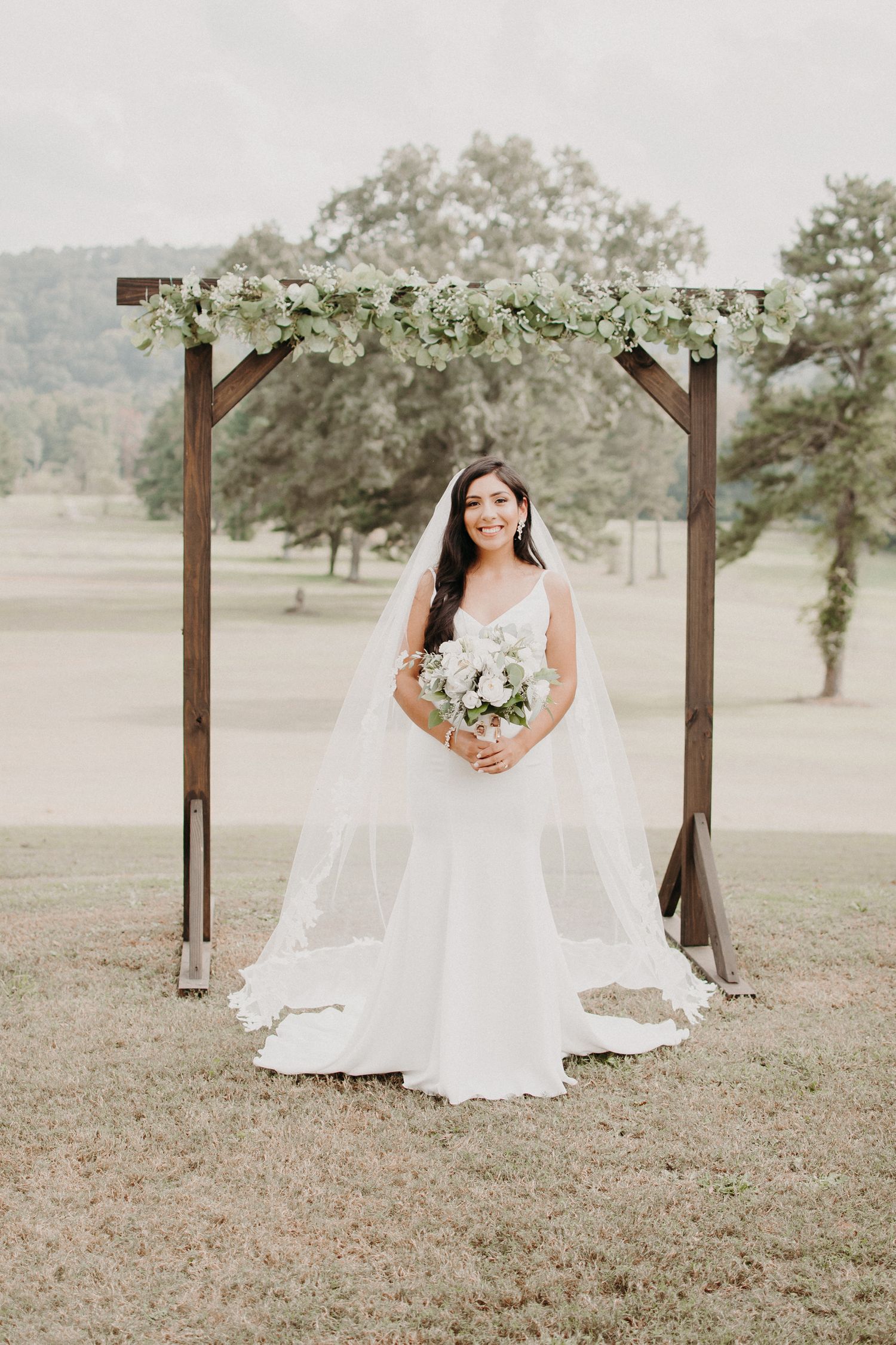 White floral wedding arch with elegant bridal portrait in an outdoor garden setting.