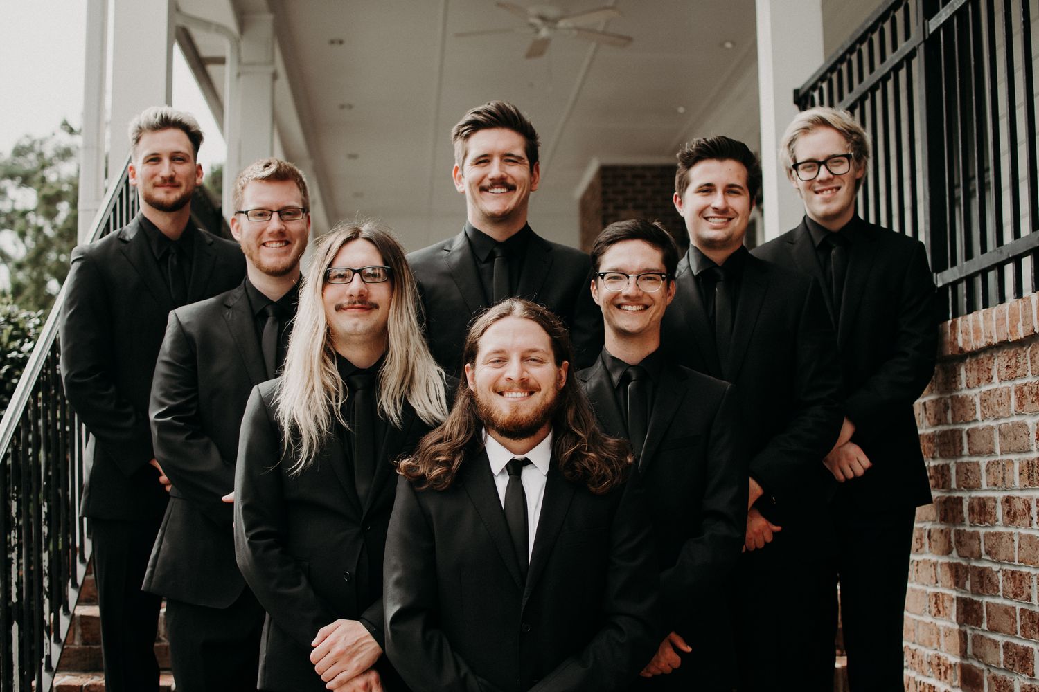 Wedding band members in black formal attire pose together on steps.