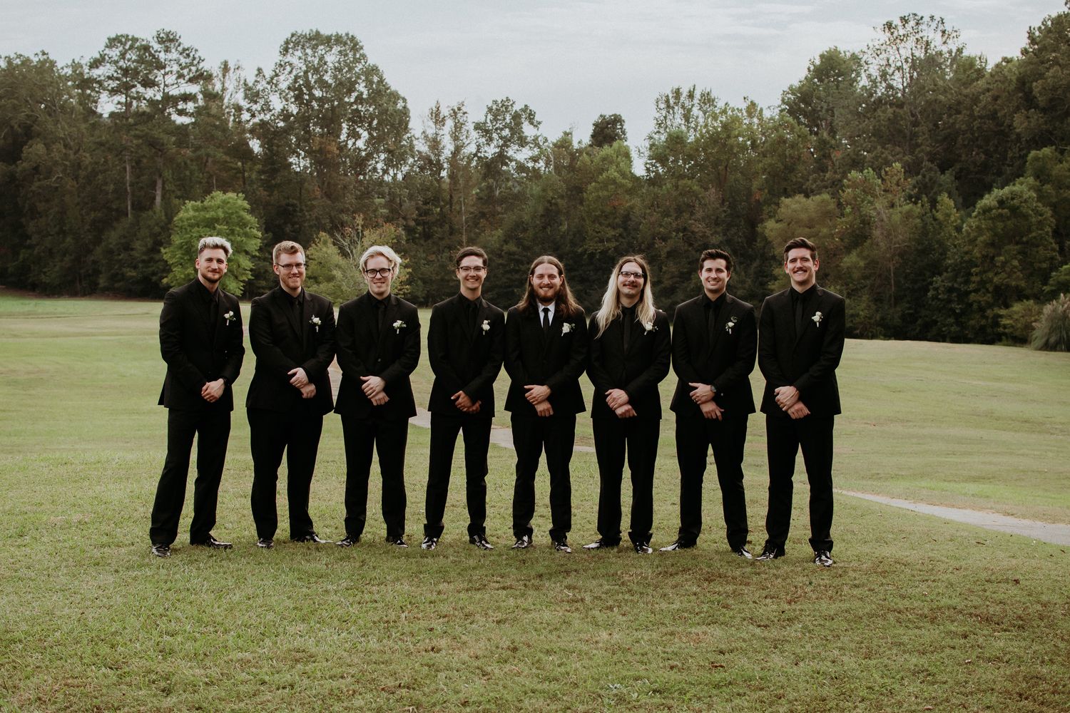 Groomsmen in black suits stand in a row on a golf course.