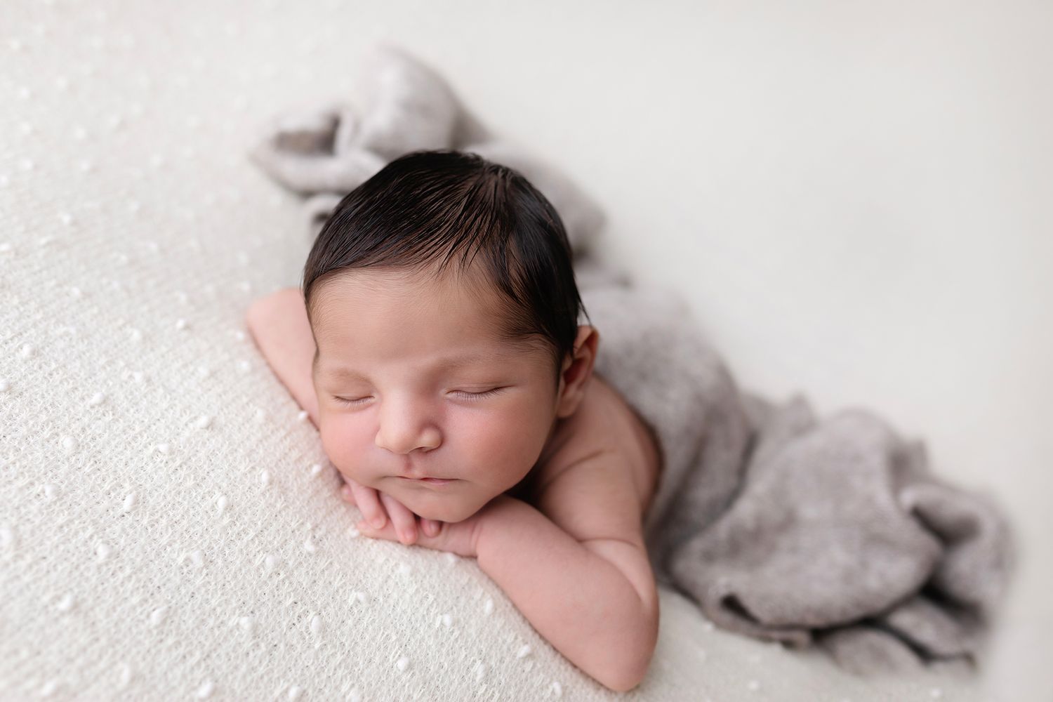 Serene newborn resting on cozy grey fabric against light background.