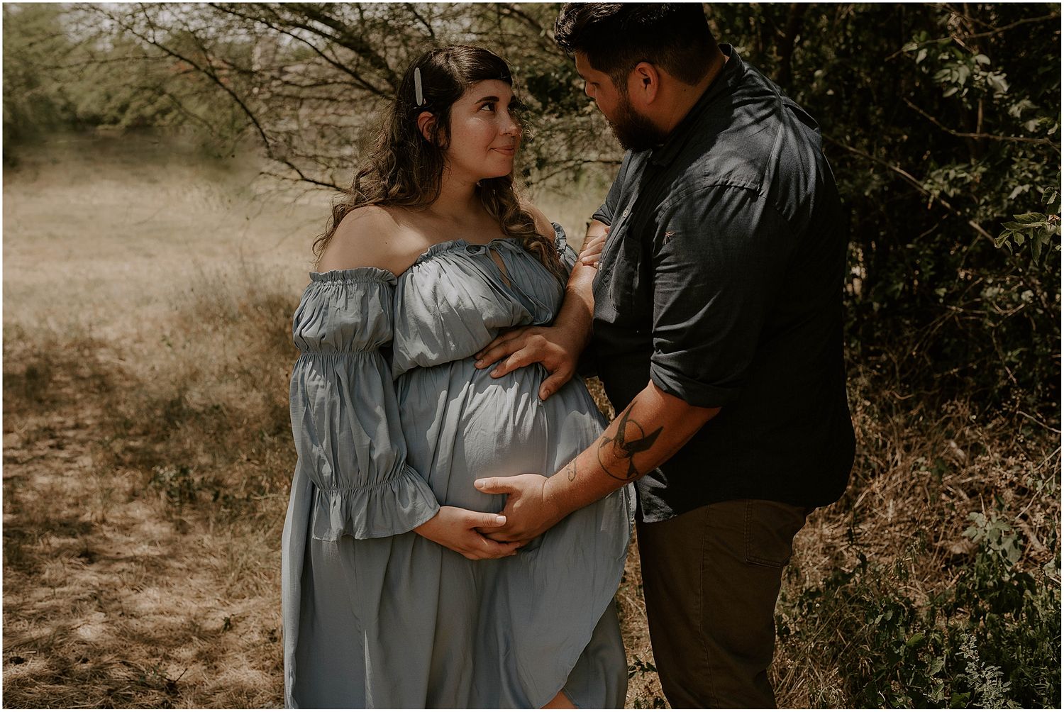 Artistic maternity photo capturing tender moment between couple in muted natural tones.