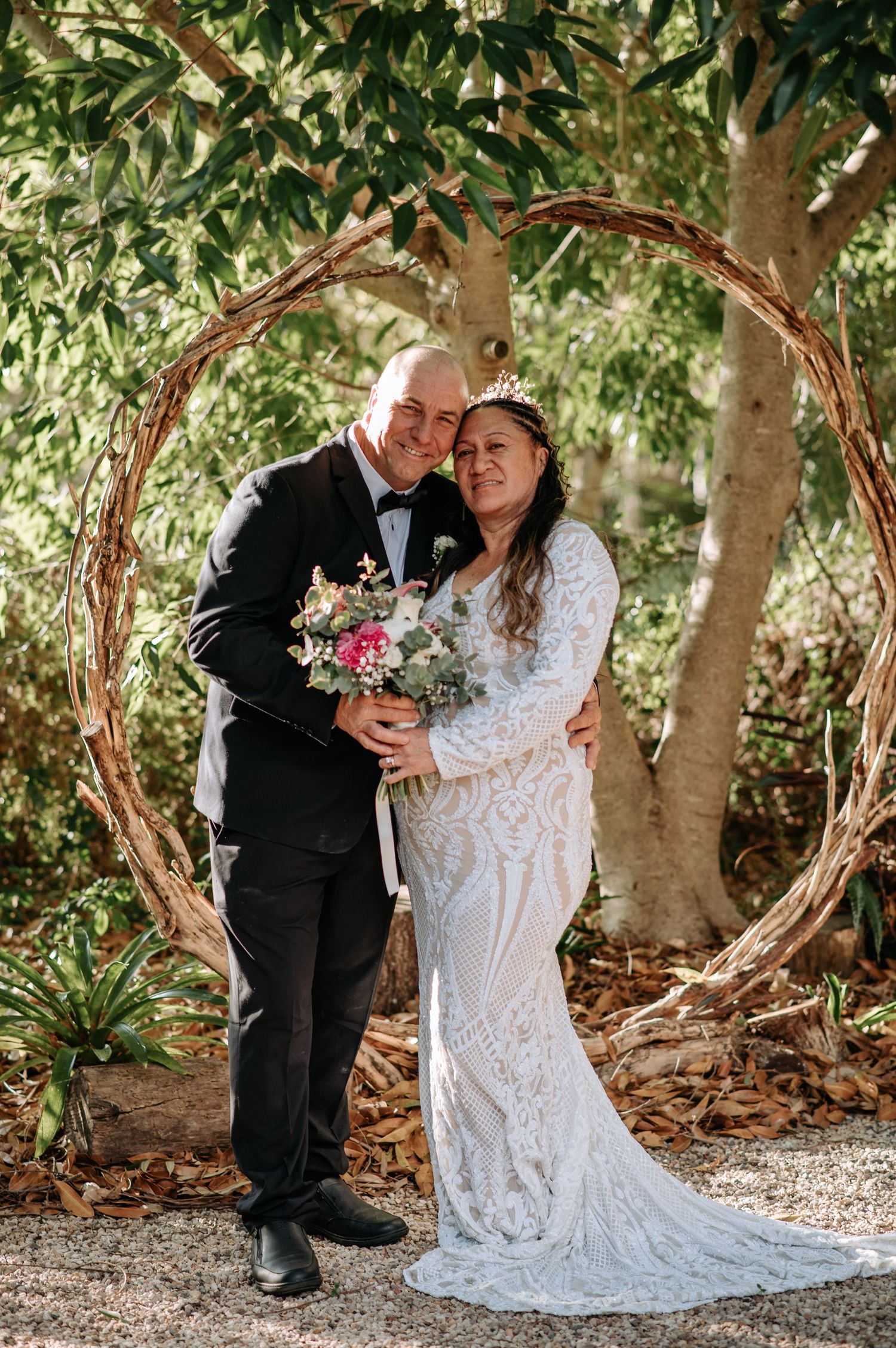 Couple poses within rustic wooden arch during garden wedding ceremony.