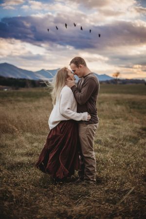 Romantic couple embracing in a golden field at sunset with mountains in the background.