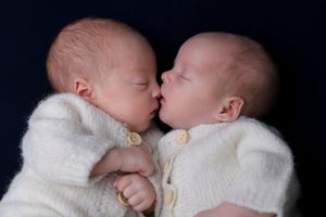 Two sleeping newborns in white sweaters touching noses in an intimate portrait.