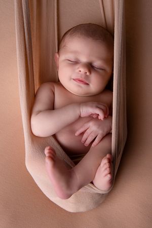 Sleeping newborn peacefully resting in beige fabric hammock.