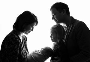 Black and white silhouette of family gazing at newborn in intimate moment.