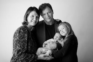 Family portrait with newborn against white background in casual attire.