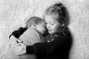 Black and white portrait showing tender embrace between two siblings on textured background.