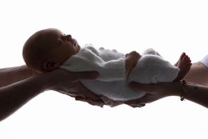 Silhouette of hands holding sleeping newborn baby wrapped in cloth.
