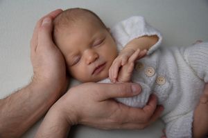 Peaceful sleeping newborn cradled gently in adult hands.