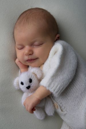 Sleeping newborn in white outfit cuddling small plush bunny toy.