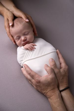 Overhead view of sleeping newborn baby in white onesie with hands gently cradling.