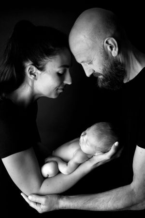 Intimate black and white portrait of new parents cradling their sleeping newborn baby.