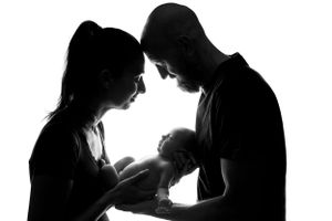 Silhouette of parents looking down at their newborn baby against white background.