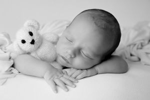 Sleeping newborn with white plush toy in monochrome portrait.