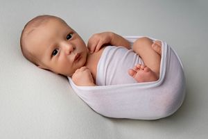 Baby wrapped in soft white swaddle blanket looking to the side.
