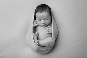 Peaceful sleeping newborn wrapped in gray swaddle against neutral background.