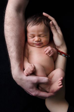 Newborn peacefully sleeping in gentle embrace against dark background.