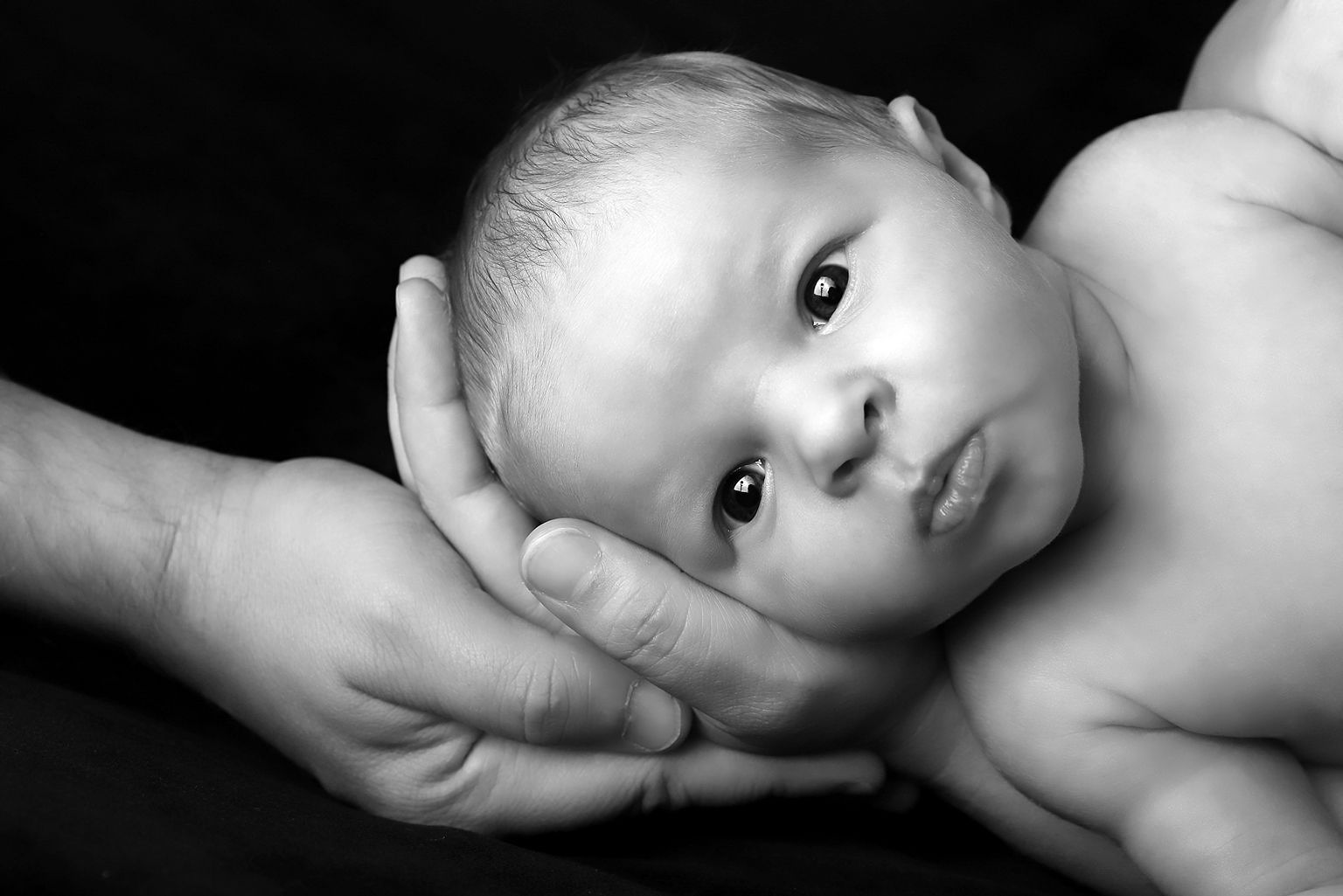 Portrait en noir et blanc d'un nouveau-né dans les mains de ses parents..