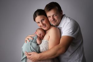 Portrait de famille tendre avec un nouveau-né enveloppé dans une douce couverture vert d'eau.