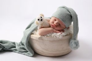 Nouveau-né endormi avec un bonnet vert menthe, niché dans un bol rustique avec une peluche.
