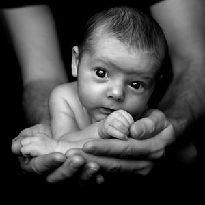 Gros plan en noir et blanc d’un bébé soutenu par des mains d’adulte.