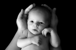 Portrait en noir et blanc d'un nourrisson avec les mains encadrant son visage.