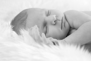 Nouveau-né paisiblement endormi sur une douce couverture en fourrure blanche dans une ambiance monochrome rêveuse.