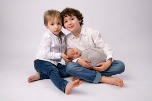 Portrait de famille avec des frères et un nouveau-né en tenues blanches sur le sol du studio.