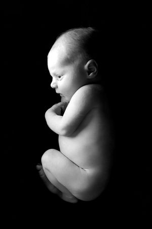 Profil artistique en noir et blanc d'un nouveau-né nu sur un fond sombre.