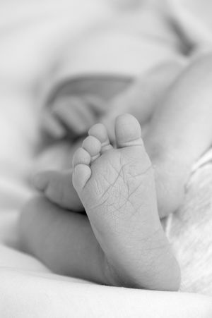 Gros plan en noir et blanc d'un petit pied de bébé avec de délicates rides et orteils, contre un fond blanc doux.