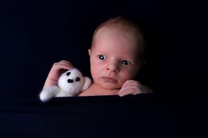 Portrait de bébé avec une petite peluche, contre un fond sombre, éclairé en lumière tamisée.