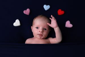 Bébé posé avec des décorations en forme de cœurs colorés, contre un fond bleu marine sombre.