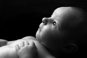 Vue de profil d’un nourrisson en noir et blanc, en lumière rasante contre un fond sombre.