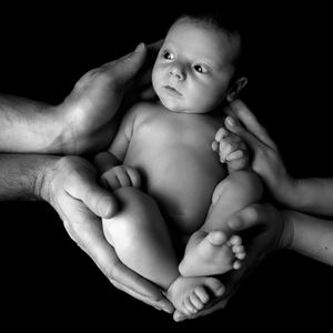 Nourrisson soutenu par les mains des parents dans un portrait  en noir et blanc.
