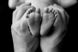 Gros plan en noir et blanc de petits pieds de bébé tenus dans les mains du papa.