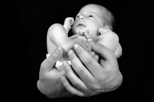 Mains délicates berçant un nouveau-né en photographie noir et blanc.