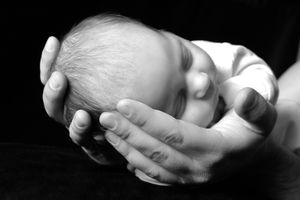 Photo artistique en noir et blanc d'un petit bébé endormi, bercé dans les mains du papa.