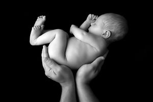 Image en noir et blanc d’un nouveau-né étant délicatement soutenu par des mains qui le soulèvent