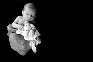 Portrait monochrome d’un nouveau-né blotti avec une petite peluche sur un fond sombre.