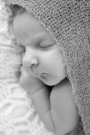 Gros plan d'un bébé endormi, emmailloté dans une délicate couverture texturée, en noir et blanc.