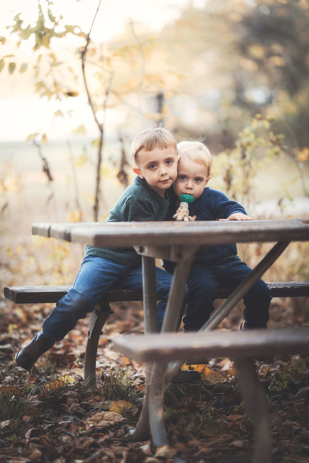Children sitting at wooden picnic table surrounded by fallen autumn leaves.