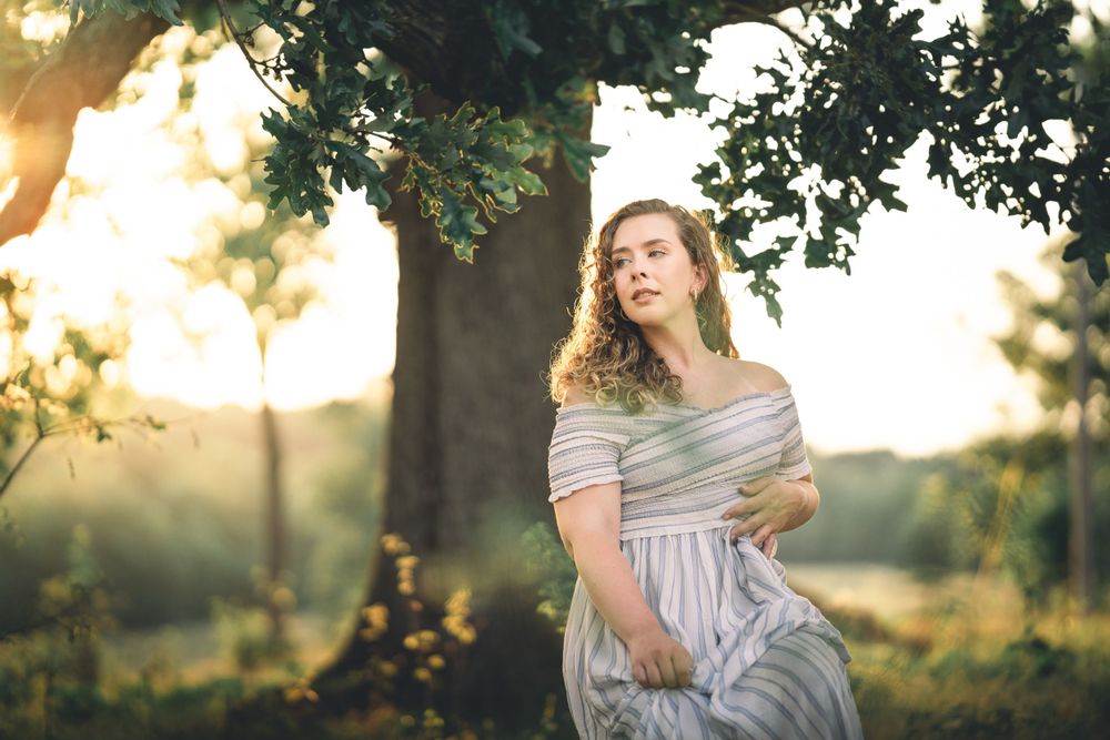 Dreamy outdoor maternity photo session in a sunlit field with flowing white dress.