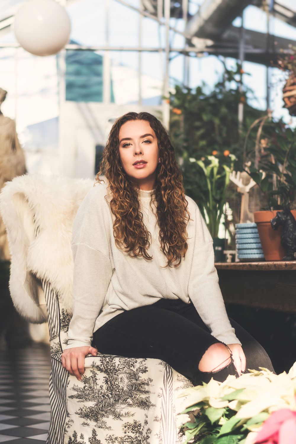 Indoor greenhouse portrait with white sweater and flowers in soft natural lighting.