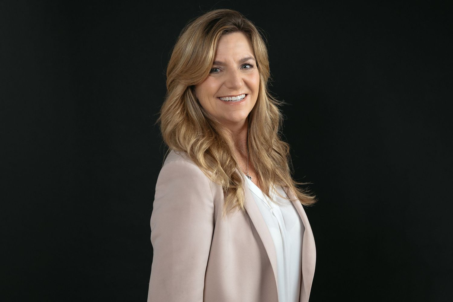 Professional headshot of a person wearing a light pink blazer against a dark background.