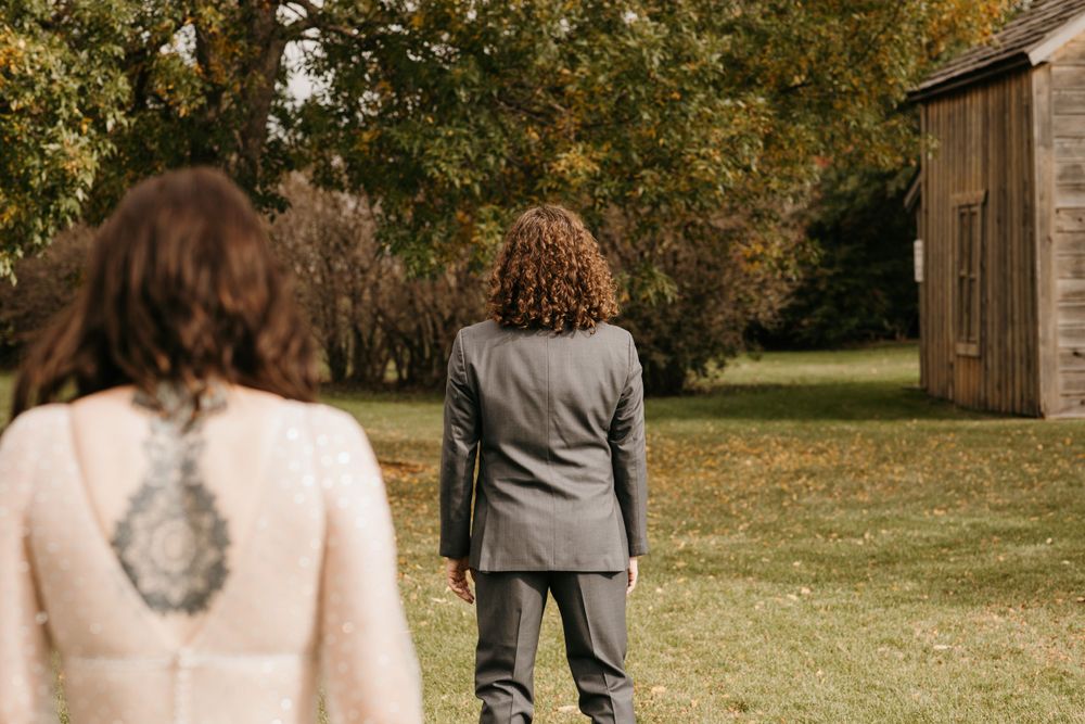 Bride in lace gown approaches groom in gray suit for first look in autumn garden.